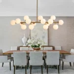 Modern 16-light linear dining chandelier with milk white glass globes installed over a large wooden dining table.