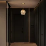 A mini crystal pendant light with gold finish illuminating a stylish dark hallway entrance.
