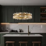Modern crystal chandelier installed above a kitchen island with dark green cabinetry.