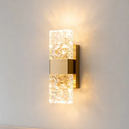 Brass wall sconce with two textured crystal shades and warm LED lighting on a neutral wall