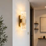 Modern brass wall sconce with textured crystal shades lighting a hallway near a doorway