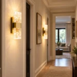 Two modern brass wall sconces illuminating a residential hallway with warm light