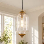 Clear glass pendant light with a ribbed lantern shade and decorative bronze finish hanging in a bright interior.