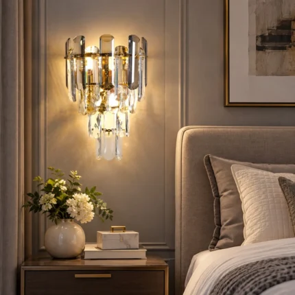 Crystal wall sconce with tiered smoke gray and clear crystals beside an upholstered bed.