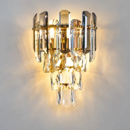Front view of an illuminated smoke gray and clear crystal wall sconce with cascading crystal tiers.