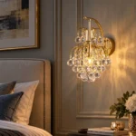 Gold crystal wall sconce Style B with cascading round crystal drops, illuminated beside an upholstered bed
