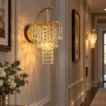 Illuminated Style C crystal wall sconce with gold curved arms and hanging crystals in an elegant hallway