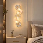 Five-flower glass wall sconce glowing above a bedside table in a neutral bedroom