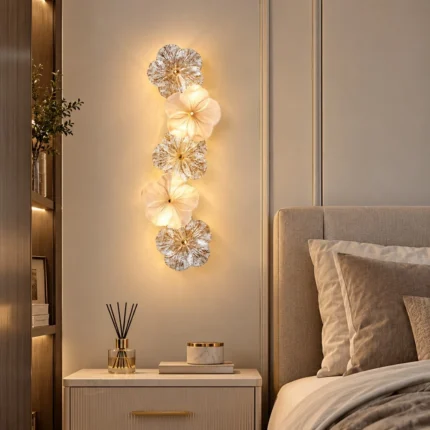 Five-flower glass wall sconce glowing above a bedside table in a neutral bedroom