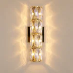 Hardwired wall sconce in gold with four stacked crystal sections and warm decorative wall lighting