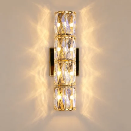 Hardwired wall sconce in gold with four stacked crystal sections and warm decorative wall lighting