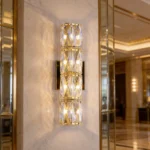 Gold crystal wall sconce with four stacked crystal sections mounted on a marble wall