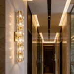 Gold crystal wall sconce with six illuminated sections in a modern hallway with stone walls