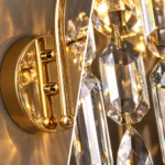 Close-up of polished gold round wall plate, curved metal arm and hanging faceted crystals on a wall sconce