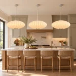 Three Japanese lantern pendant lights with glowing white oval shades arranged above a marble kitchen island