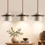 Three wabi sabi pendant lights with textured stone shades hanging above a round wooden table in a neutral living room.