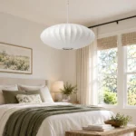 White Japanese pendant light with oval ribbed shade installed above a bed in a bright neutral bedroom